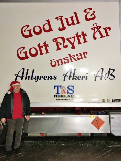 En bild på Håkan Ahlgren i tomteluva framför en av sina lastbilar där det står God Jul & Gott nytt år önskar Ahlgrens Åkeri AB (Bifab) på flaket