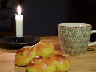 Bild på ett ljus, en kopp och några lussebullar