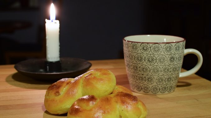 Bild på ett ljus, en kopp och några lussebullar